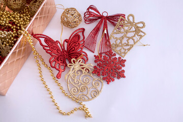 Caja con adornos navideños rojos y dorados para el árbol de Navidad sobre fondo blanco.