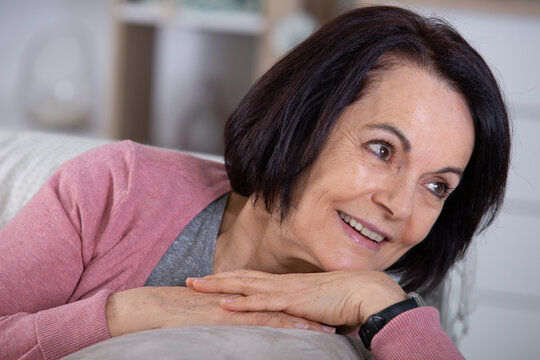 portrait of relaxed older woman smiling and sitting on sofa