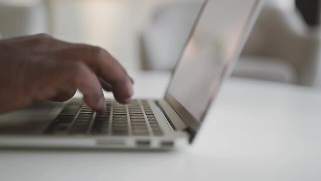 Unrecognizable african american senior man typing on laptop keyboard at home, black male hands working on computer