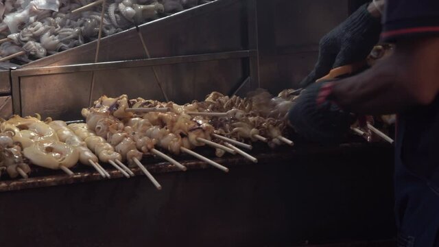 Grilled squids preparing for customer. Fresh squid in stick grill on street food in Bangkok, Thailand.