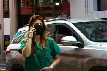 A nurse in the city talking with a smartphone. A beauty nurse smiling in the city while passing...