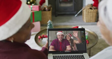 Smiling diverse senior female friends using laptop for christmas video call with couple on screen - Powered by Adobe