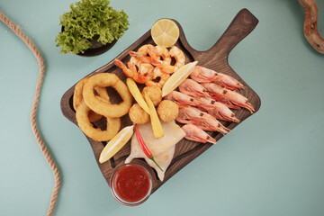 Seafood dishes with fried squid rings, shrimp and onion rings, garnished with lemon on a cutting board on a wooden background.