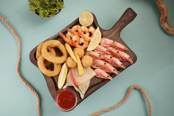 Seafood dishes with fried squid rings, shrimp and onion rings, garnished with lemon on a cutting board on a wooden background.