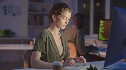 Waist-up stab shot of young female programmer drinking coffee to stay awake while working on computer in office late at night - Powered by Adobe