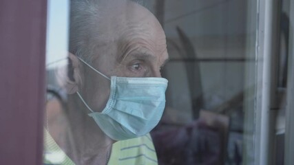 Close side view of elderly man in face mask looking behind window glass. Social distancing and lockdown concept. Depressed people during corona virus pandemic. - Powered by Adobe