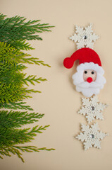santa Claus's face made of felt against the background of green thuja branches and a decor of white snowflakes with a place for text in vertical format