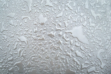 Irregular patterned water drops on a silver-coloured shiny metal surface
