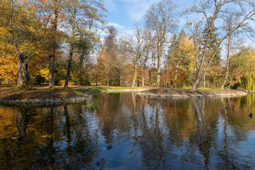 Fototapeta na wymiar Castle park - autumn landscape with sun with colorful trees. Blue sky with white clouds.