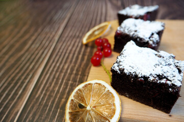 three pieces of gluten-free brownie with red currants lie on a wooden board with slices of dried lemon. gluten-free, lactose-free brownies