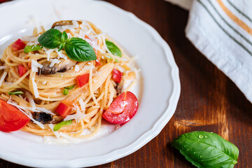 Fresh pasta with spaghetti, tomato, mushrooms, basil and parmesan cheese in white plate on a wooden background with ingredients in background