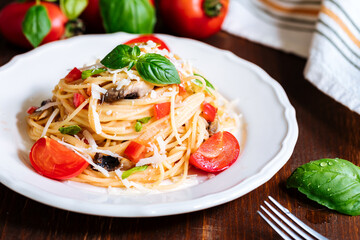 Fresh pasta with spaghetti, tomato, mushrooms, basil and parmesan cheese in white plate on a wooden background with ingredients in background