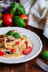 Fresh pasta with spaghetti, tomato, mushrooms, basil and parmesan cheese in white plate on a wooden background with ingredients in background