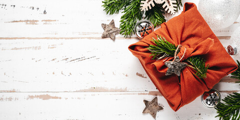 Gift in eco friendly reusable fabric package furoshiki on white wooden background. Banner with copy space