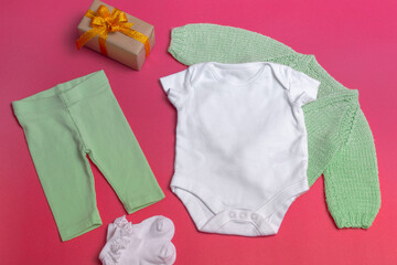 On a colored background, a blank white baby bodysuit close-up - with a knitted green jacket and green leggings - a mockup of clothes for newborns. copy space