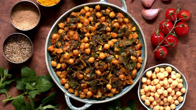 Chickpea dish in bowl with ingredients and spices around. Vegan cuisine. Table spin.