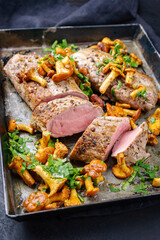 Fried dry aged pork fillet chateaubriand medallion steak natural with chanterelles and parsley served as close-upon a rustic metal tray on black background © HLPhoto