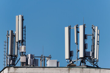 Mobile phone base station or cell tower atop of a building against a blue sky on a sunny day