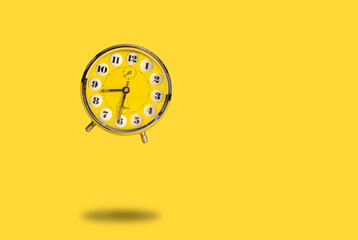 Round yellow alarm clock flying above the ground as a concept for time flies or wake up alarm on a bright yellow background with space for copy