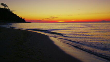 Lake coastline at orange sunset dawn. Dark sea beach with mountain silhouette