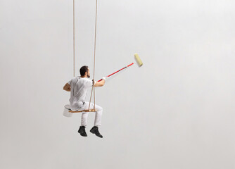 Painter sitting on a swing and painting a wall