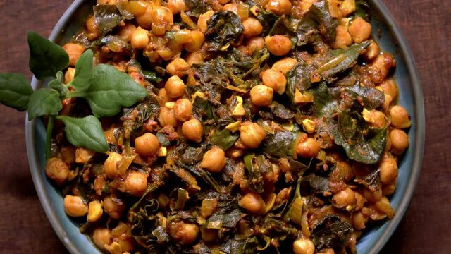 Close view of chickpea dish in bowl with spinach leaves. Vegan cuisine. Table spin.