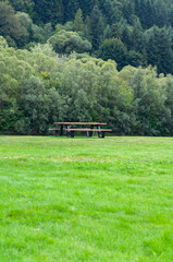 Wooden bench and table on green lawn near чriver among mountains and dense forest