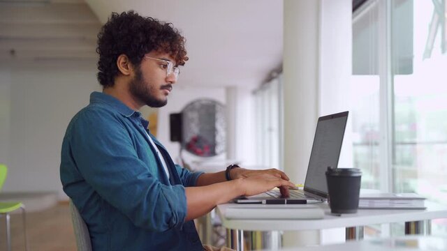 Indian man IT professional freelancer working using laptop computer at office