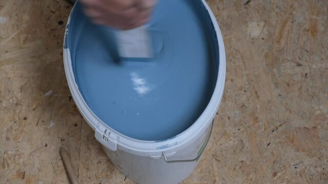 The hands of a man with a stick stir the paint in a bucket Blue paint drips into the bucket Home repair 
