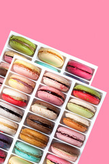 Two tray of different macarons or macaroons with varied flavors on pink background. Top view, copy space