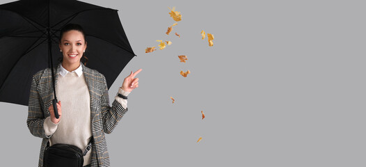 Stylish young woman in autumn clothes and with umbrella on grey background with space for text