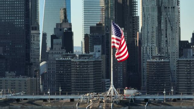 flying left view of American flag atop Brooklyn Bridge with NYC passing in bkrd