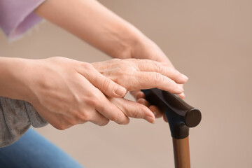 Hands of young woman and her grandmother with walking stick at home