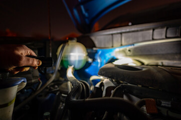 Shining a light into the open hood of vehicle to check the engine
