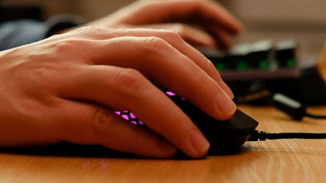 Controlling the game using a modern gaming rgb mouse and a mini keypad. A man plays with two hands on new equipment.