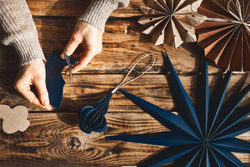 Winter holiday decoration. Woman's hands making christmas paper snowflakes, paper blue stars and fans made of craft paper on wooden table. Nature aesthetic. Zero waste handmade gifts. DIY.