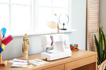 Modern tailor's workplace with sewing machine and sketches near window