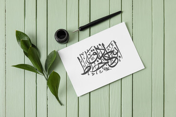 Paper with Arabic text and tools for calligraphy on wooden background