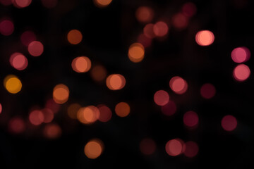 Defocused bokeh lights on black background, abstract naturally blurred backdrop for Christmas eve or birthday party. Festive light texture. Pink, yellow, red garland in blur. Overlay effect for design