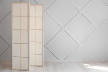 Stylish folding screen in room interior on wall background