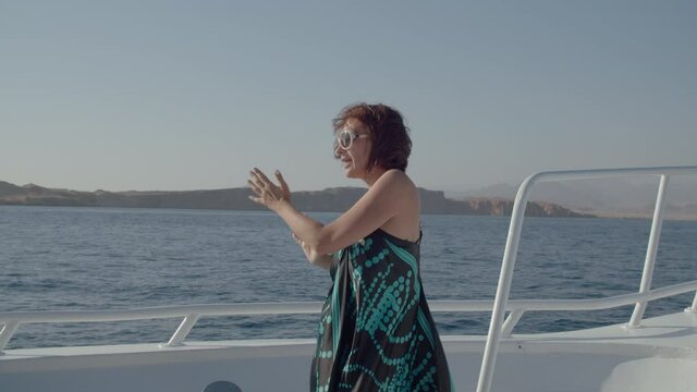 Happy woman dancing on white yacht sailing in the sea. Cheerful and positive female dances on boat.