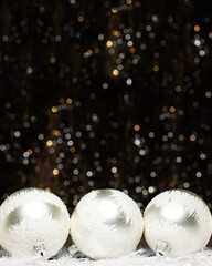 Christmas banner decorations view of three silver evening balls with white snow on it on dark background with silver colors bokeh and artificial snow. Holidays concept with copy space.