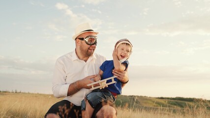 Dad, child, son play together in a toy wooden airplane in a summer park. Happy family. A child in a pilot's helmet, a dad in pilot's glasses. Baby and dad on the playground, family dreams, fantasies