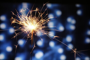 Burning Christmas sparkler against blurred lights