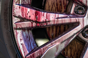 Car wheel cleaning process close up. Rim cleaner gives purple chemical reaction when removing metal...