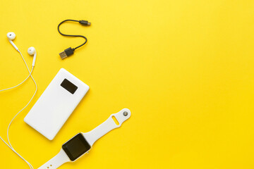 Modern power bank, smartwatch and earphones on yellow background