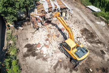 Demolition of building aerial view from drone. Excavator breaks old house.