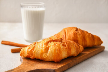 Wooden board with delicious croissants on white background