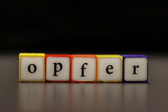 The word VICTIM (German: OPFER) written on colorful wooden cubes isolated on a black background