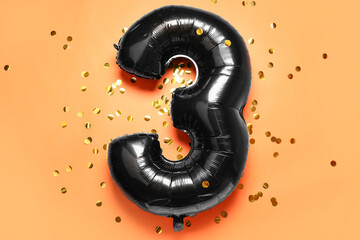 Black balloon in shape of figure 3 and confetti on orange background